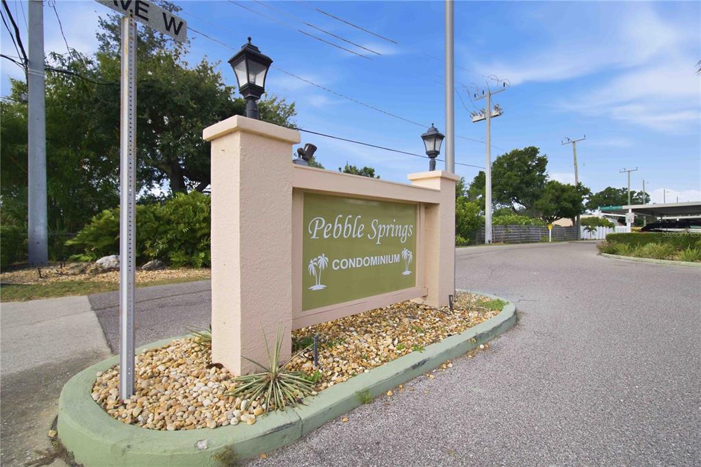 A beige monument sign for Pebble Springs Condominium stands at the entrance of a road — 6032 7TH AVENUE W UNIT 6032, BRADENTON, FL