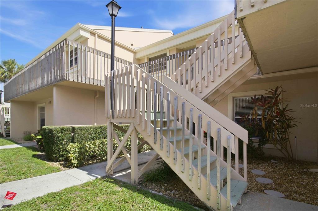 An exterior view of a two-story apartment building with a wooden staircase and balcony — 6032 7TH AVENUE W UNIT 6032, BRADENTON, FL