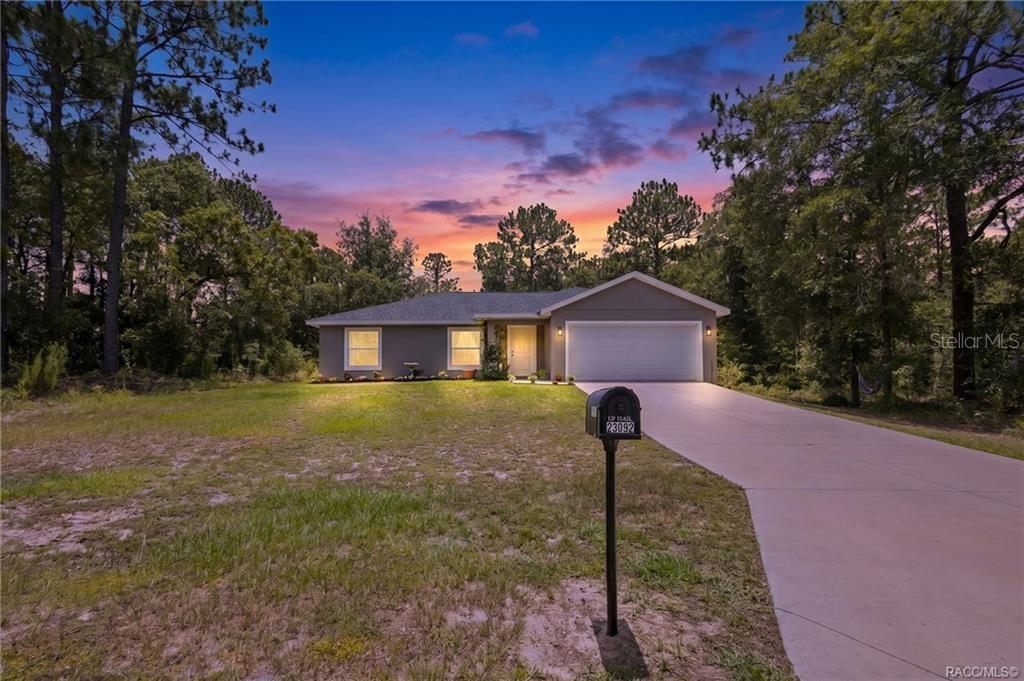 A single-story house with a two-car garage and a concrete driveway at sunset — 23092 NW SKYLARK STREET, DUNNELLON, FL
