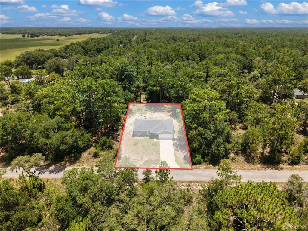 An aerial view shows a single-story house with a concrete driveway on a wooded lot — 23092 NW SKYLARK STREET, DUNNELLON, FL