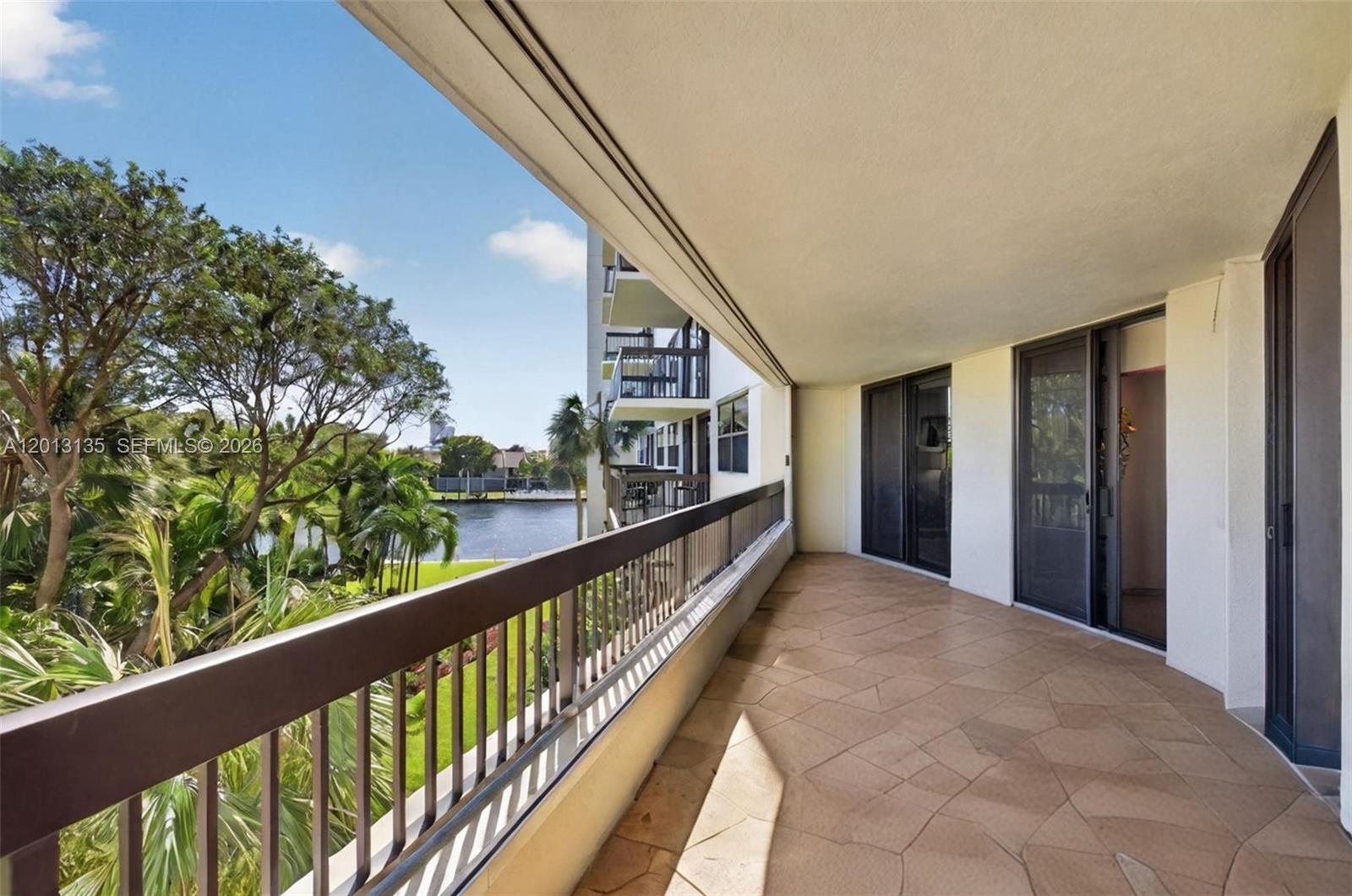 A covered balcony with stone flooring overlooks a canal and lush tropical landscaping — 2900 NE 14th St Cswy # 304, Pompano Beach FL 33062, POMPANO BEACH, FL