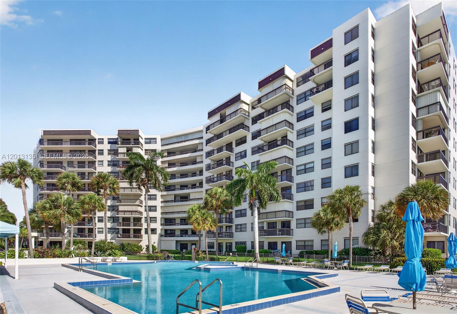 A multi-story apartment building overlooks a swimming pool with palm trees and lounge chairs — 2900 NE 14th St Cswy # 304, Pompano Beach FL 33062, POMPANO BEACH, FL