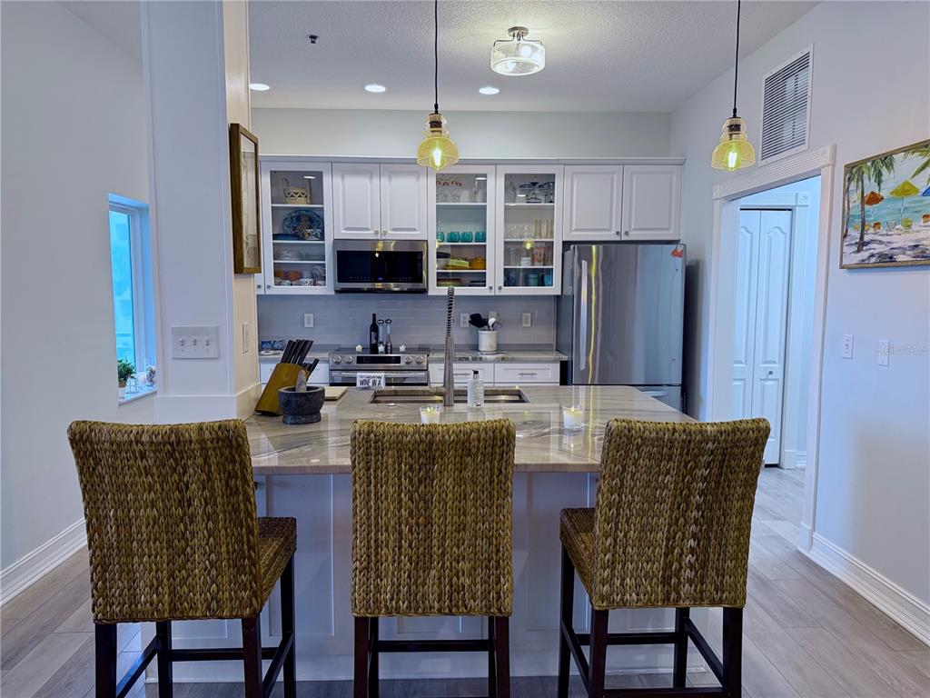 A kitchen features a central island with bar stools, white cabinetry, and stainless steel appliances — 423 S ATLANTIC AVENUE UNIT 102, NEW SMYRNA BEACH, FL