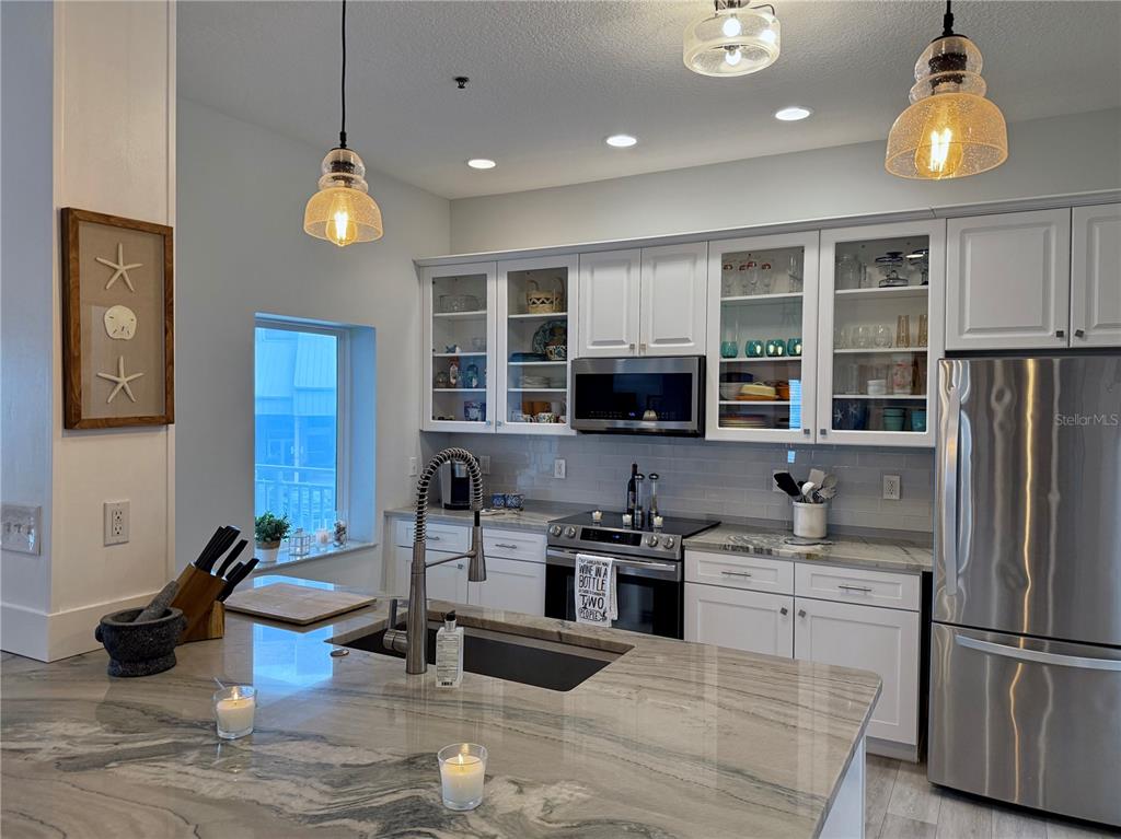 A modern kitchen features white cabinetry, stainless steel appliances, and a large stone-topped island — 423 S ATLANTIC AVENUE UNIT 102, NEW SMYRNA BEACH, FL