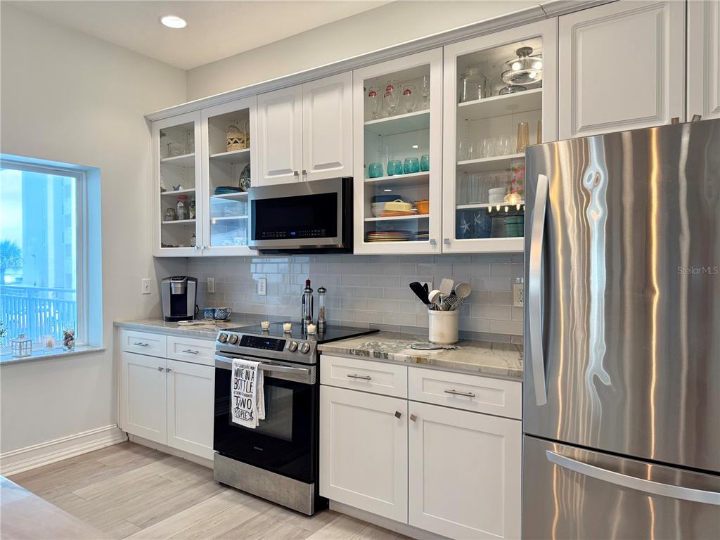 A kitchen features white cabinets, stainless steel appliances, a glass-tile backsplash, and light-colored countertops — 423 S ATLANTIC AVENUE UNIT 102, NEW SMYRNA BEACH, FL