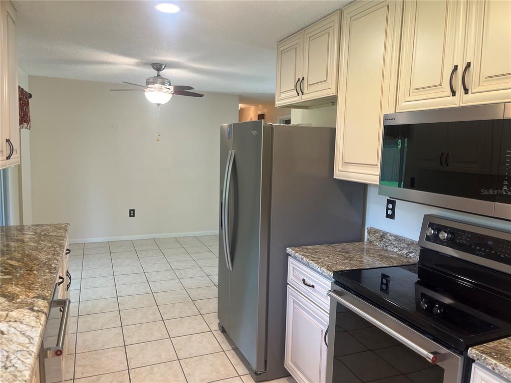 A kitchen features light-colored cabinets, granite countertops, a stainless steel refrigerator, and tile flooring — 5455 NE 22ND AVENUE, OCALA, FL