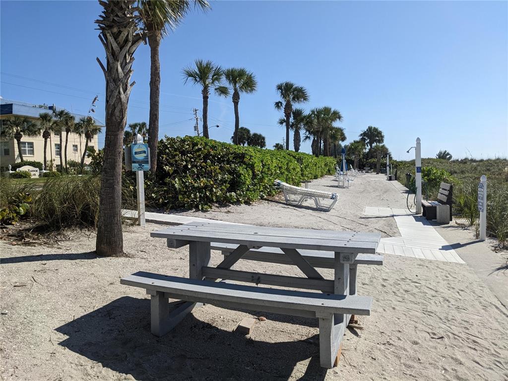A gray picnic table sits on a sandy beach area with palm trees and lounge chairs — 3806 GULF OF MEXICO DRIVE UNIT C208, LONGBOAT KEY, FL