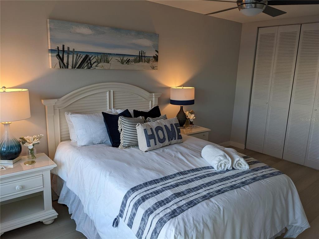 A bedroom features a white bed with blue accents, two nightstands, and a coastal painting — 3806 GULF OF MEXICO DRIVE UNIT C208, LONGBOAT KEY, FL