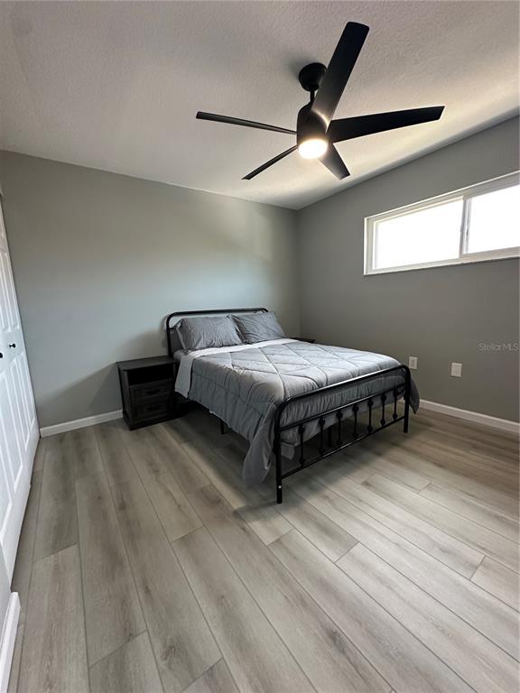 A bedroom features gray walls, light wood-look flooring, a black metal bed frame, and a ceiling fan — 460 E BASE AVENUE UNIT 129, VENICE, FL