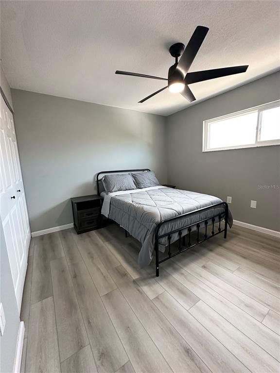 A bedroom features light wood-look flooring, gray walls, a black metal bed frame, and a ceiling fan — 460 E BASE AVENUE UNIT 129, VENICE, FL
