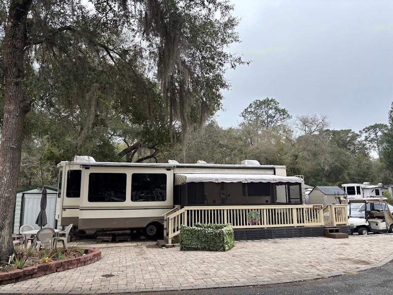 A large recreational vehicle with an attached wooden deck sits on a paved lot — 14432 252ND COURT ROAD NE UNIT 140, FORT MC COY, FL
