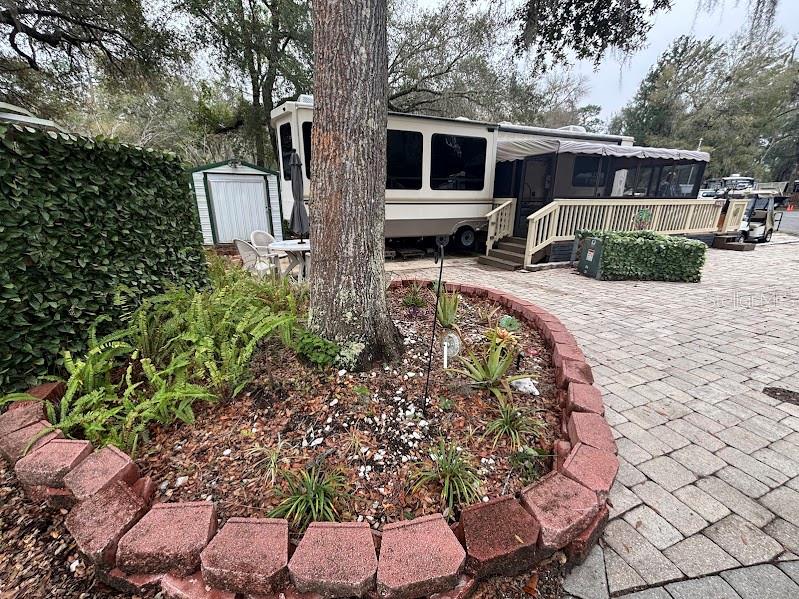 A large tree stands in a landscaped bed next to a recreational vehicle and deck — 14432 252ND COURT ROAD NE UNIT 140, FORT MC COY, FL