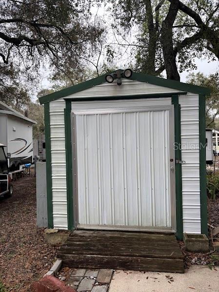 A metal storage shed with a green frame and a wooden ramp stands outdoors — 14432 252ND COURT ROAD NE UNIT 140, FORT MC COY, FL