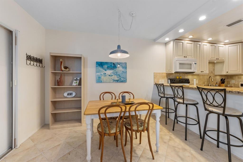A dining area with a wooden table, chairs, a bookshelf, and a kitchen breakfast bar — 117 7TH STREET N UNIT 35, BRADENTON BEACH, FL