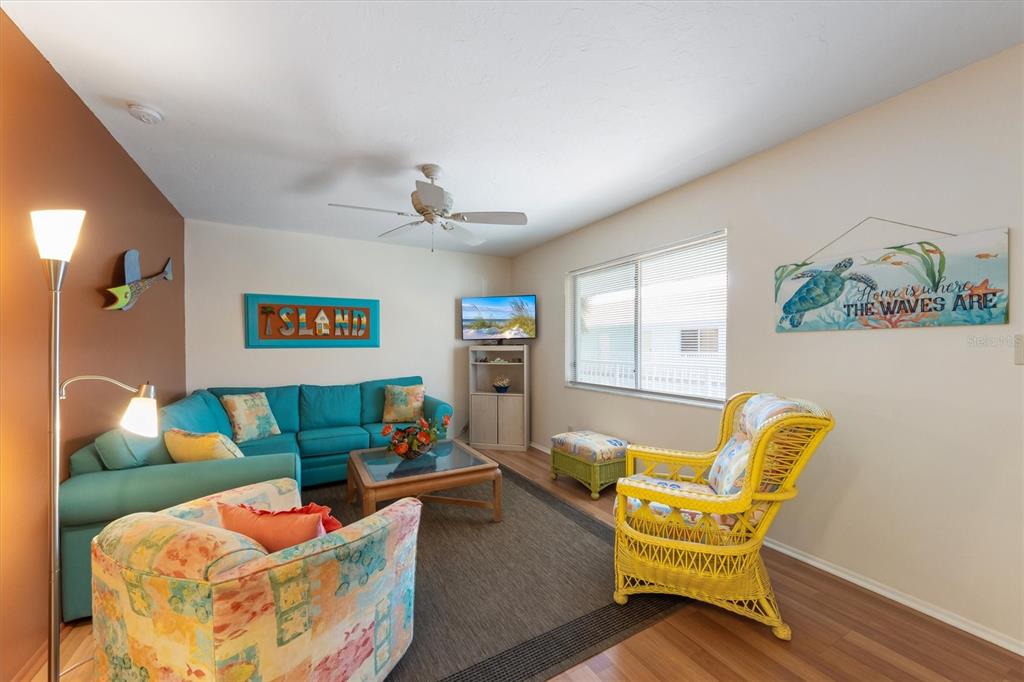 A living room features a turquoise sectional, a yellow wicker chair, and beach-themed wall decor — 117 7TH STREET N UNIT 35, BRADENTON BEACH, FL