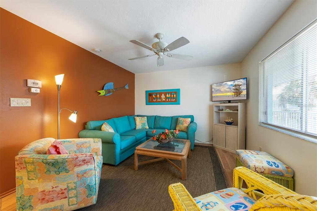A living room features a blue sectional sofa, patterned armchair, and orange accent wall — 117 7TH STREET N UNIT 35, BRADENTON BEACH, FL