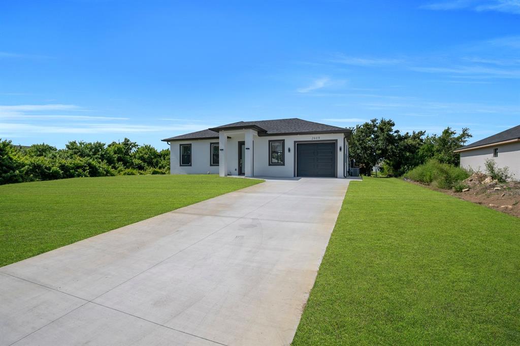 A single-story house with a white exterior, dark roof, and concrete driveway under a blue sky — 2609 21ST STREET SW, LEHIGH ACRES, FL