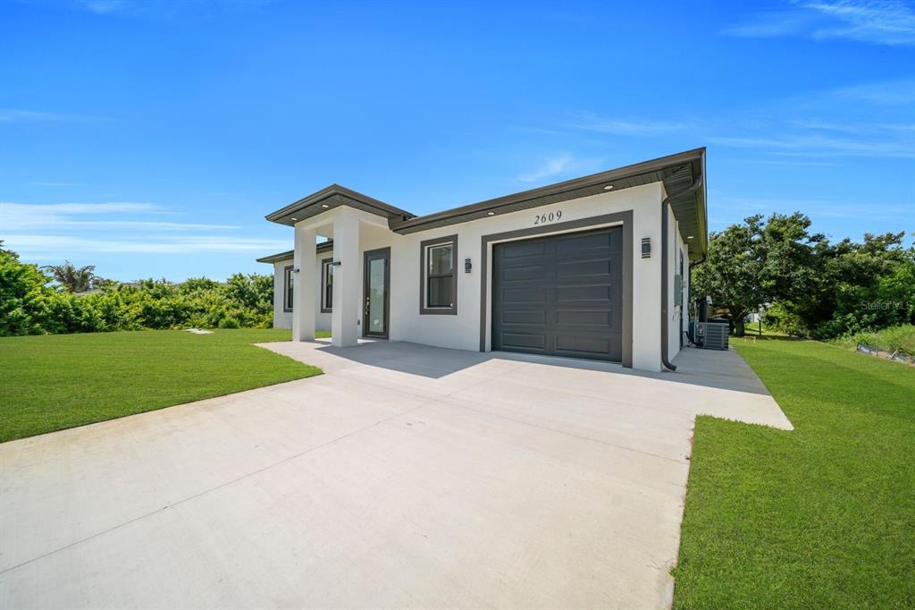 A modern single-story house with a white exterior, dark garage door, and concrete driveway — 2609 21ST STREET SW, LEHIGH ACRES, FL
