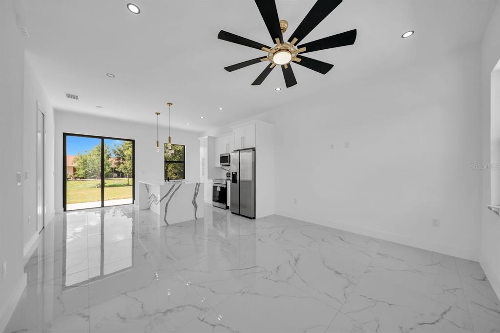 A modern open-concept kitchen and living area features white marble-look tile floors and cabinetry — 2609 21ST STREET SW, LEHIGH ACRES, FL