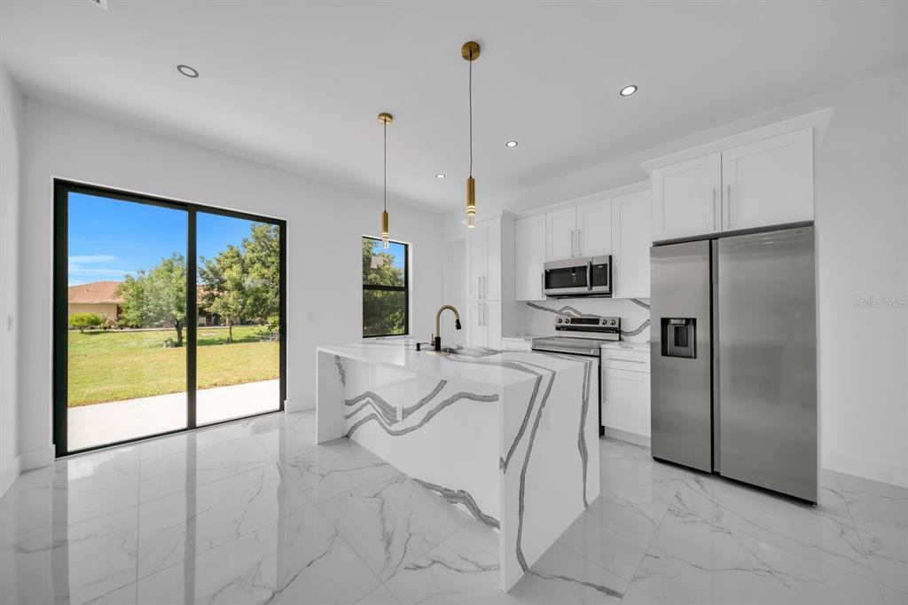 A modern kitchen features a waterfall marble island, white cabinetry, and stainless steel appliances — 2609 21ST STREET SW, LEHIGH ACRES, FL