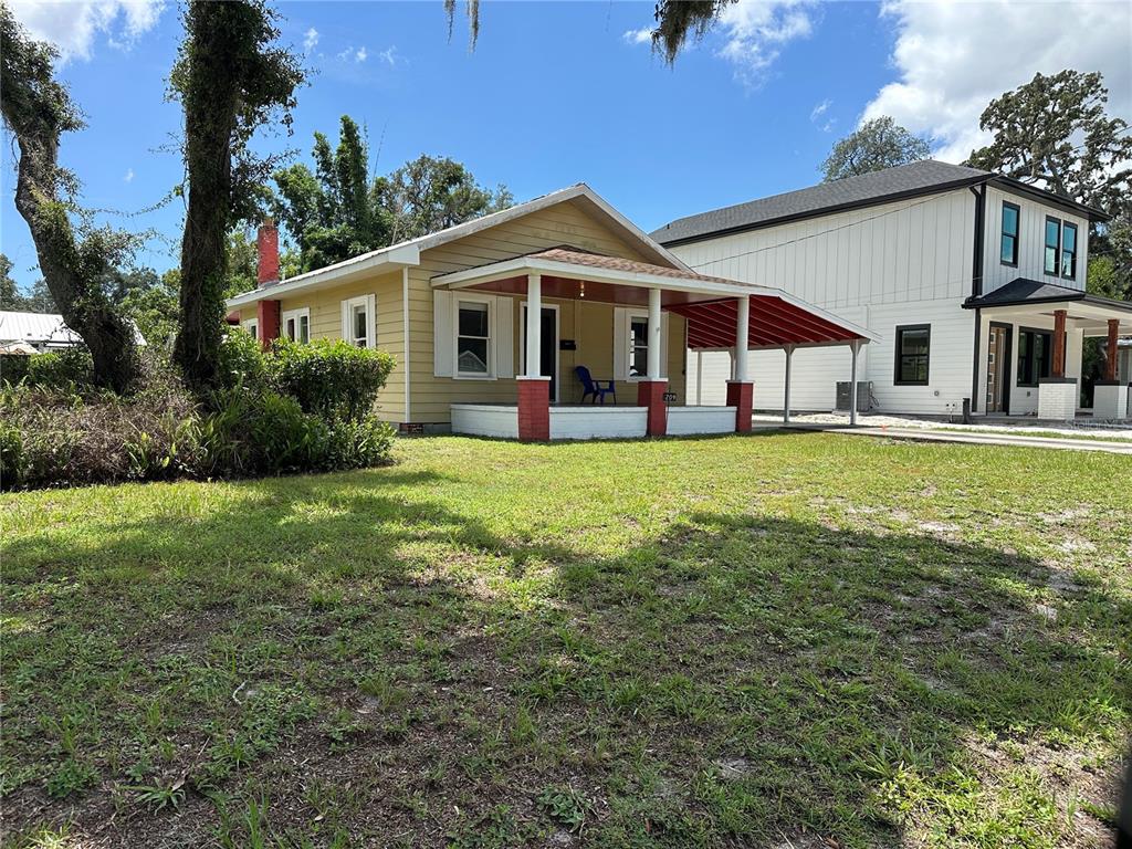 A yellow house with a front porch and attached carport sits next to a modern building — 1209 E ELLICOTT STREET, TAMPA, FL