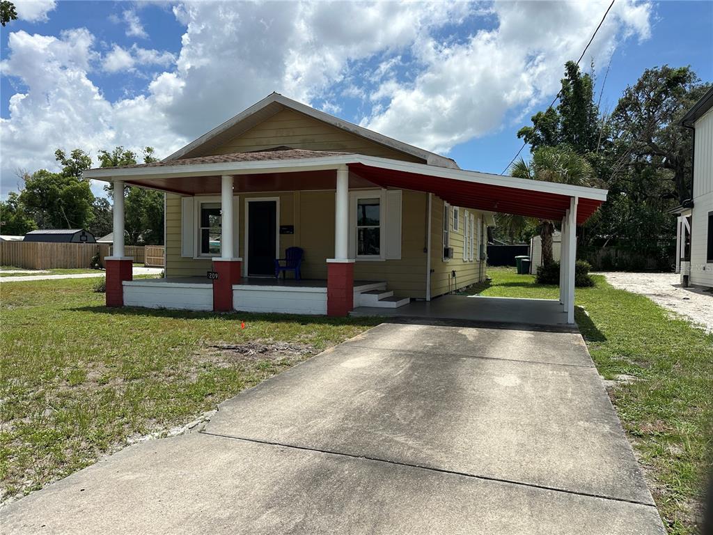 A yellow single-story house features a front porch with red accents and an attached carport — 1209 E ELLICOTT STREET, TAMPA, FL