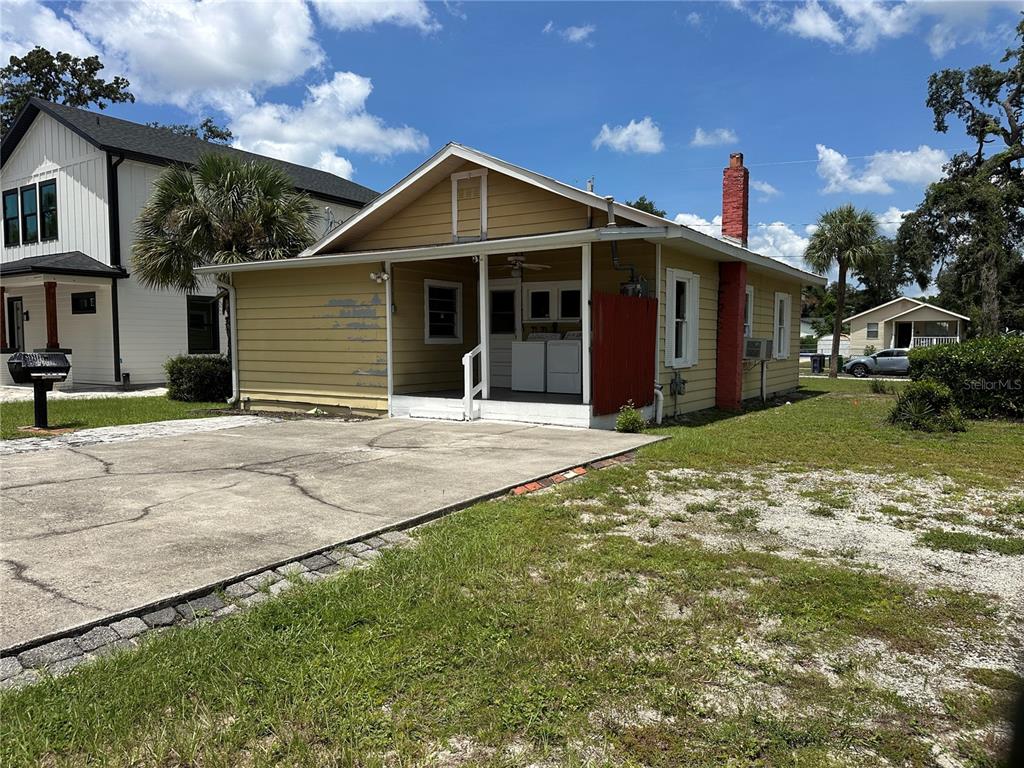 A yellow single-story house with a front porch, concrete driveway, and a red brick chimney — 1209 E ELLICOTT STREET, TAMPA, FL