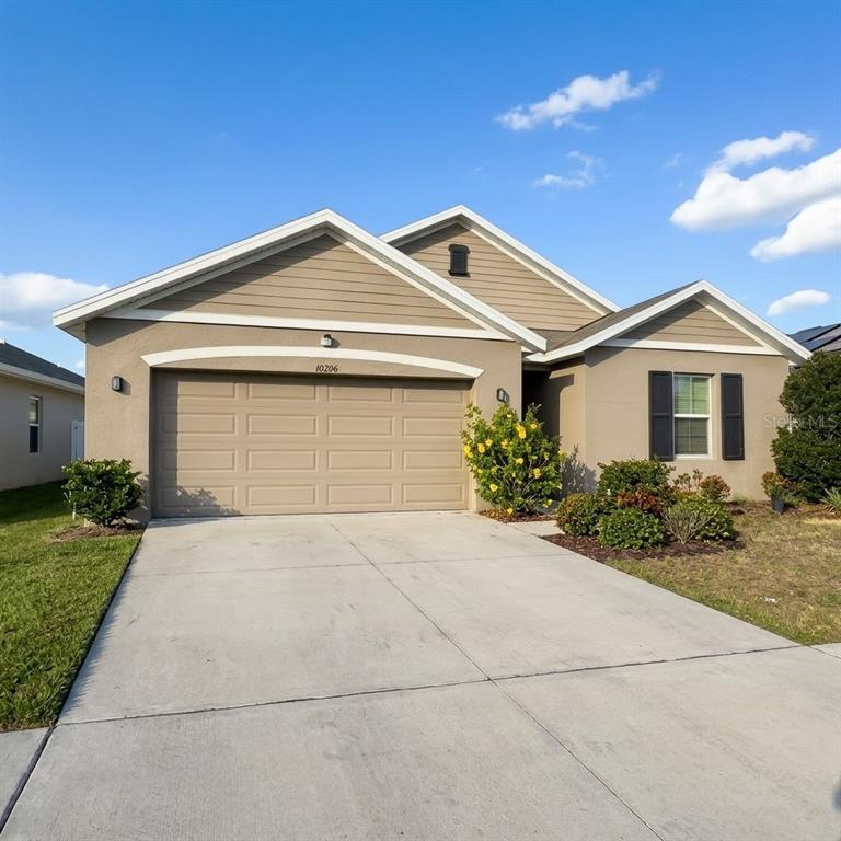 A tan, single-story suburban house features a two-car garage and a concrete driveway — 10206 GOLDEN LIGHT COURT, RIVERVIEW, FL