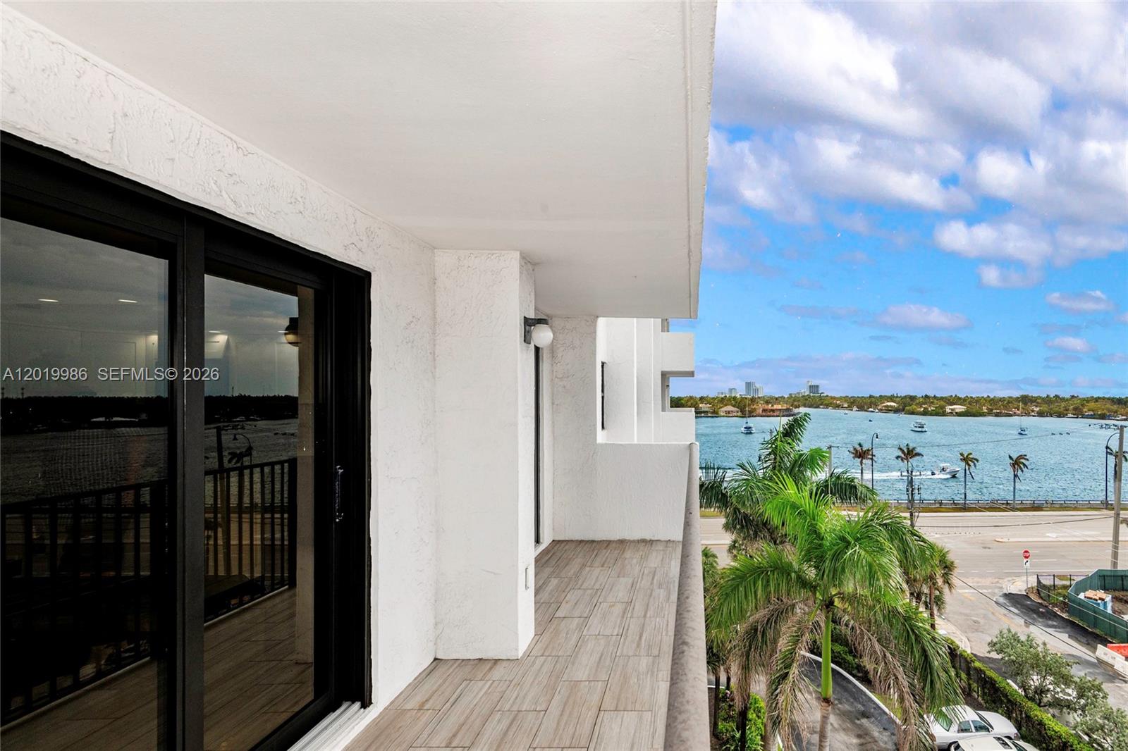A balcony with wood-look tile flooring overlooks a body of water and palm trees — 1201 S Ocean Dr # 610N, Hollywood FL 33019, HOLLYWOOD, FL