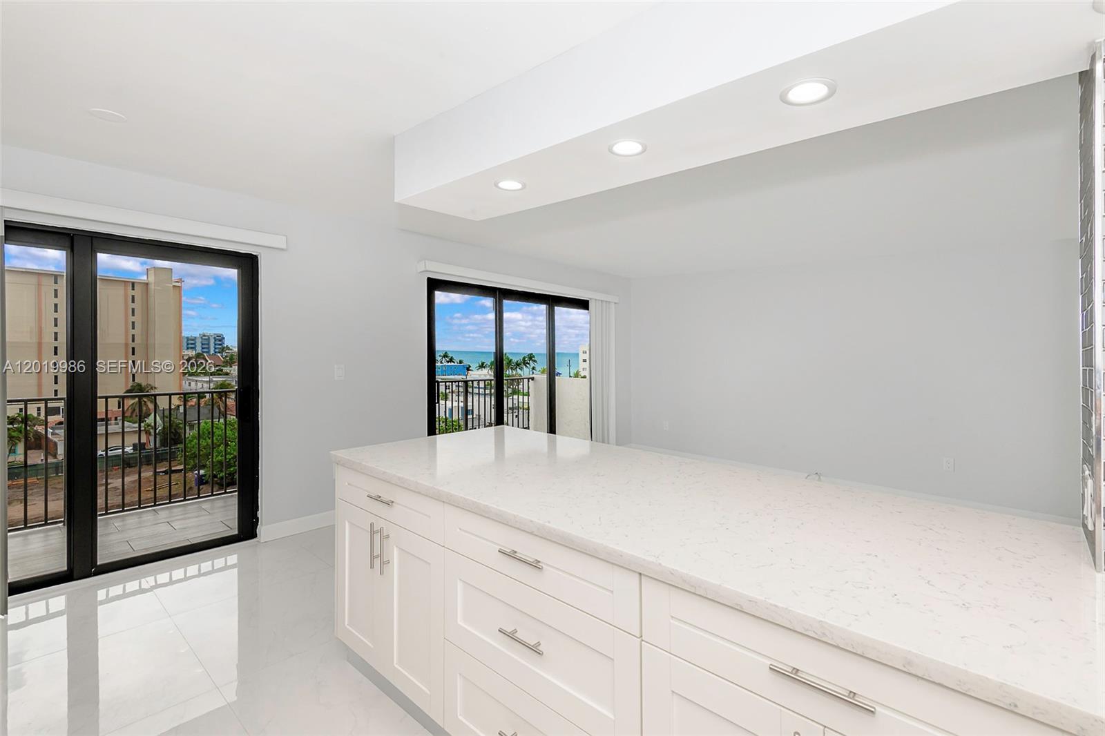 A modern kitchen island with white cabinetry and quartz countertops sits before sliding glass doors — 1201 S Ocean Dr # 610N, Hollywood FL 33019, HOLLYWOOD, FL