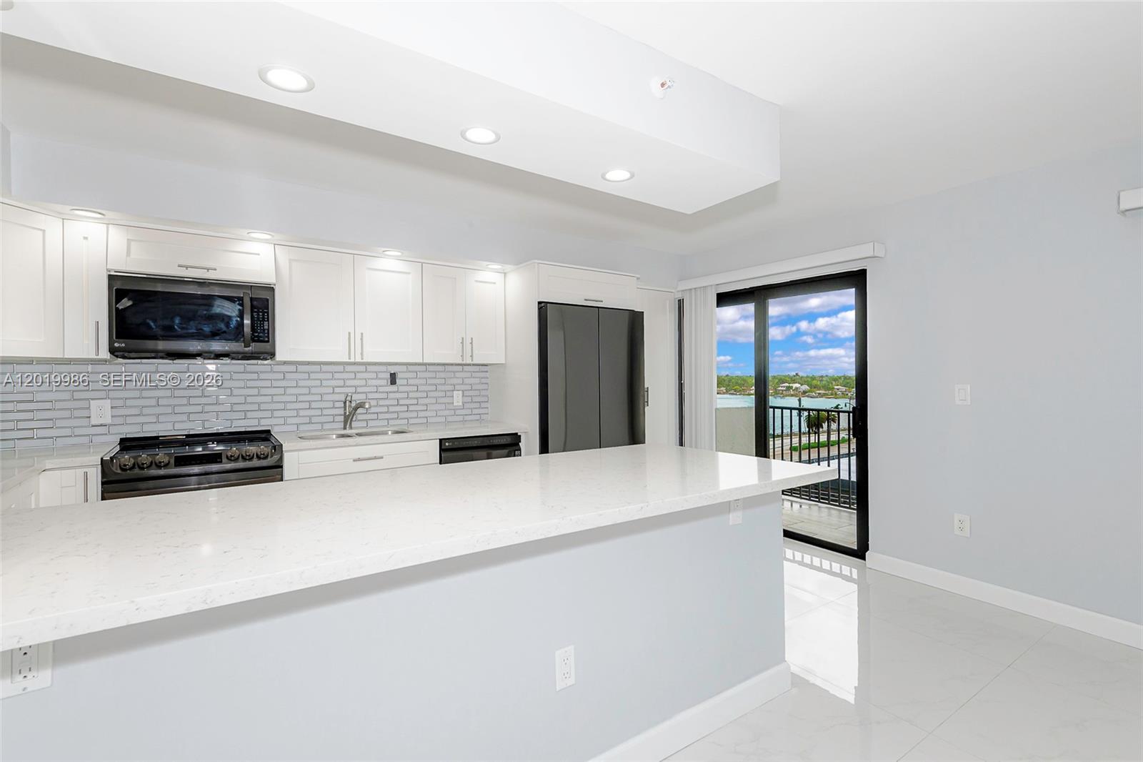 A modern kitchen features white cabinetry, a quartz island, and a sliding door to a balcony — 1201 S Ocean Dr # 610N, Hollywood FL 33019, HOLLYWOOD, FL