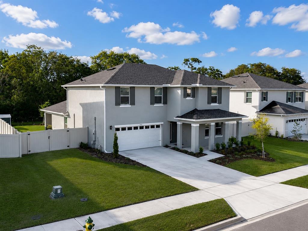 An exterior view of a two-story gray house with a white garage and lawn — 5189 GREENHEART AVENUE, MOUNT DORA, FL