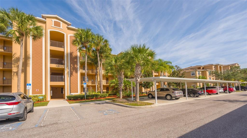 A multi-story apartment building with a covered parking area and palm trees in front — 8105 GRAND ESTUARY TRAIL UNIT 204, BRADENTON, FL