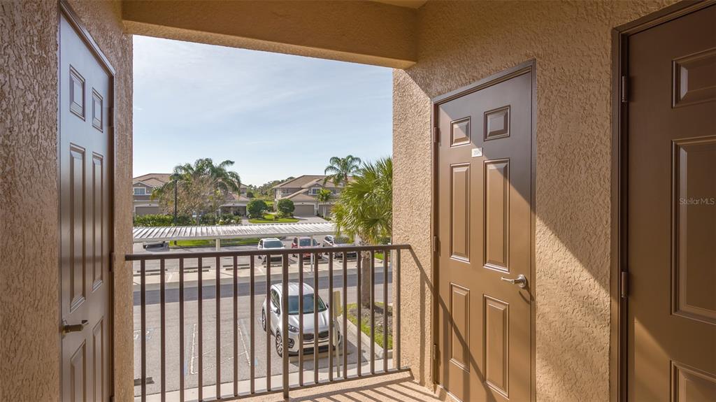 An outdoor apartment balcony with brown doors, metal railings, and a view of a parking lot — 8105 GRAND ESTUARY TRAIL UNIT 204, BRADENTON, FL