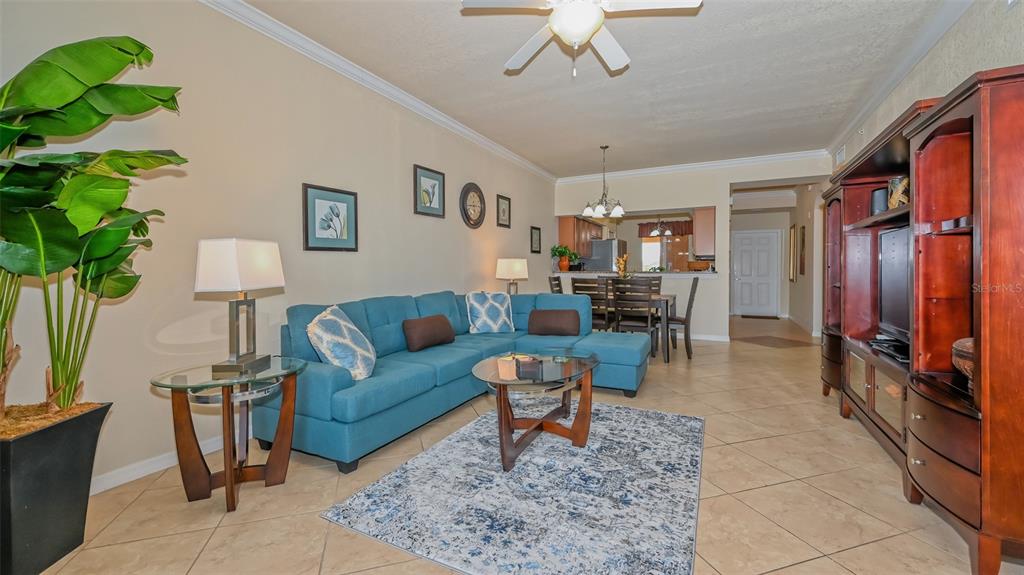 A living room features a blue sectional sofa, a glass coffee table, and tile flooring — 8105 GRAND ESTUARY TRAIL UNIT 204, BRADENTON, FL