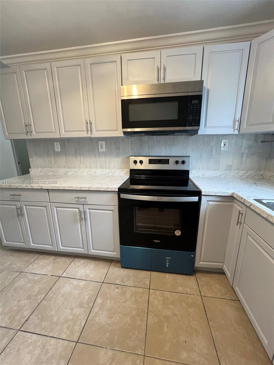 A kitchen features white cabinets, a black stove, a microwave, and light-colored countertops — 6018 Plunkett St # 1, Hollywood FL 33023, HOLLYWOOD, FL