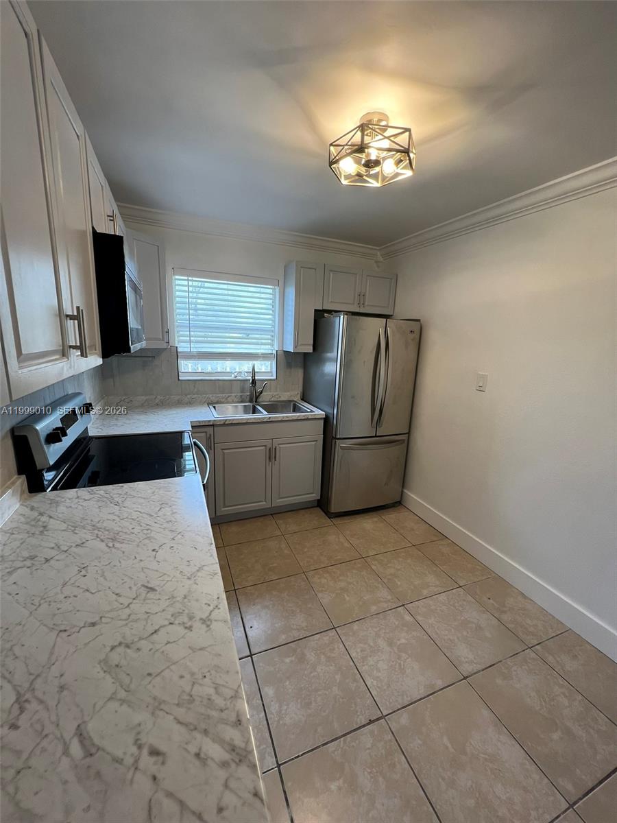 A kitchen features white cabinets, marble-patterned countertops, stainless steel appliances, and beige tile flooring — 6018 Plunkett St # 1, Hollywood FL 33023, HOLLYWOOD, FL