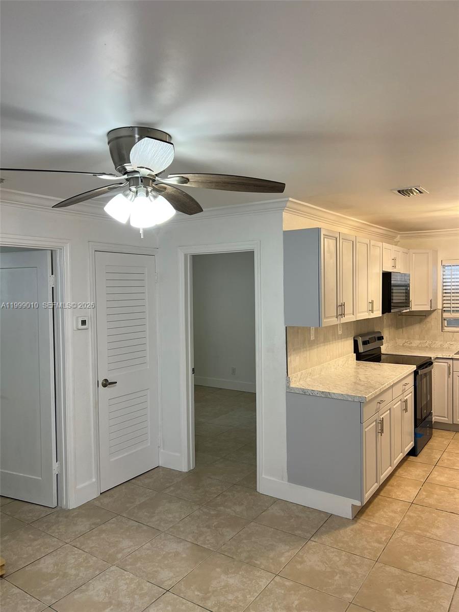 A kitchen with white cabinets and marble-look countertops sits adjacent to a tiled hallway — 6018 Plunkett St # 1, Hollywood FL 33023, HOLLYWOOD, FL