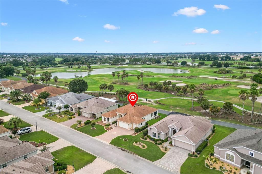 An aerial view of a single-story house with a paved driveway and golf course backdrop — 2757 DAY LILY RUN, THE VILLAGES, FL