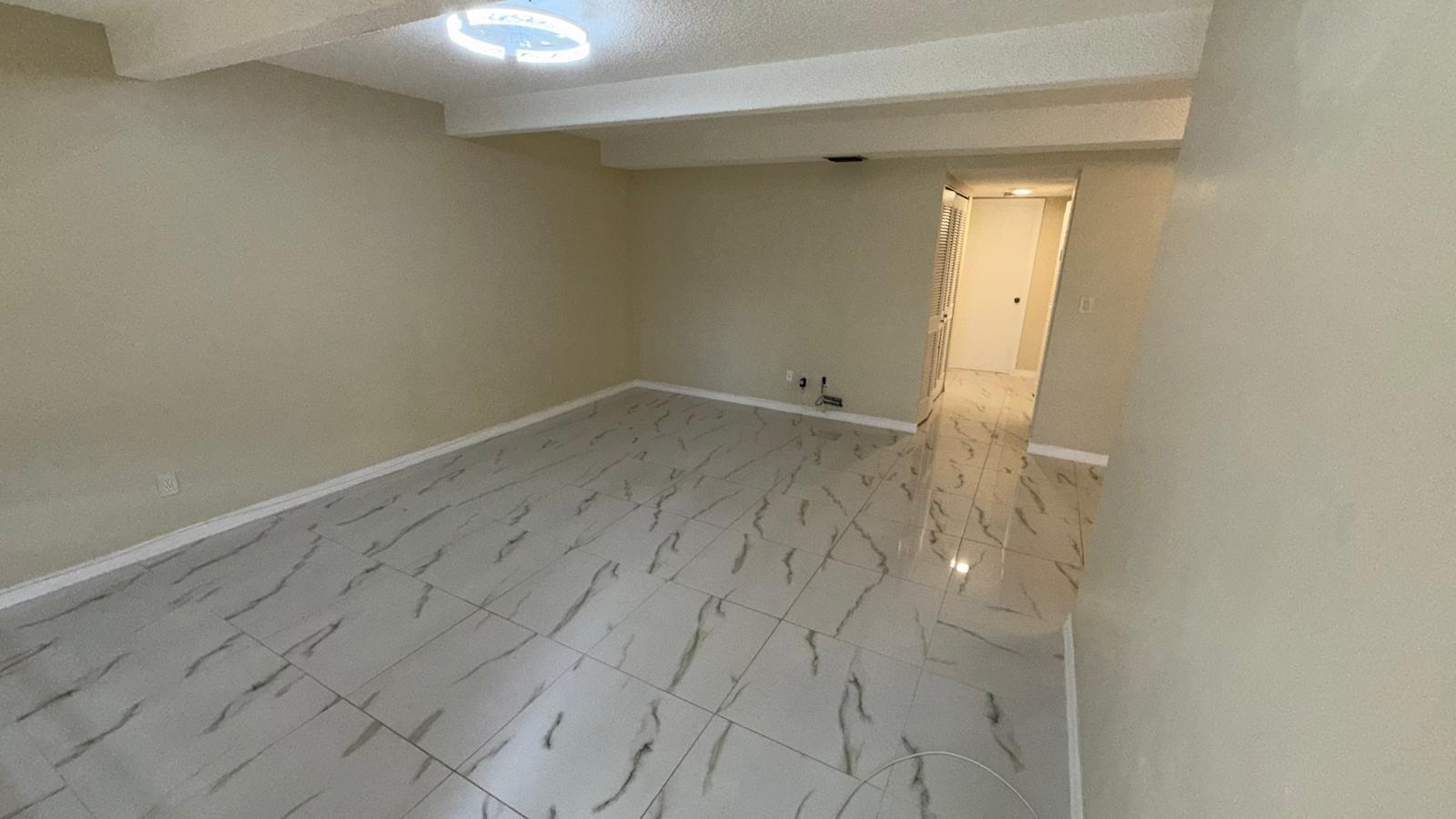 An empty room with beige walls, white ceiling beams, and light-colored marble-patterned tile flooring — 1225 S Flagler Avenue # 313, Pompano Beach FL 33060, POMPANO BEACH, FL