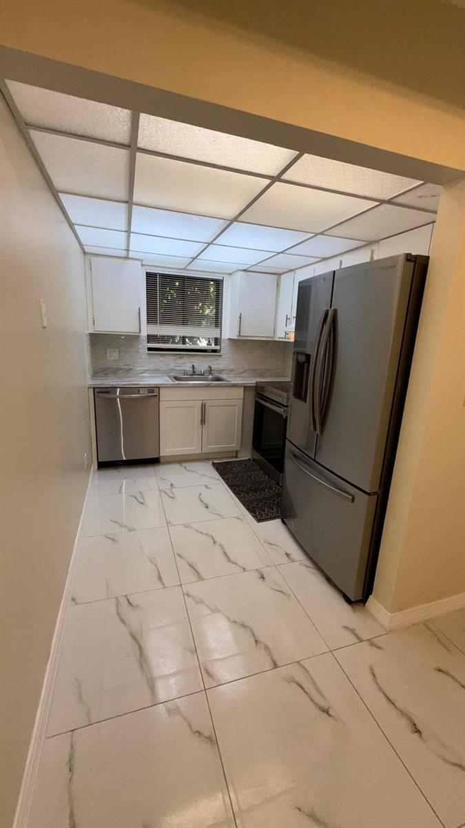 A galley kitchen features white cabinets, stainless steel appliances, and white marble-patterned tile flooring — 1225 S Flagler Avenue # 313, Pompano Beach FL 33060, POMPANO BEACH, FL