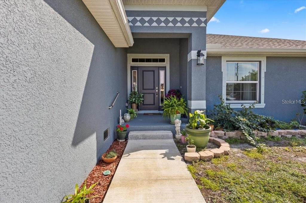 A concrete walkway leads to the covered front entryway of a gray stucco house — 15251 APPLETON BOULEVARD, PORT CHARLOTTE, FL