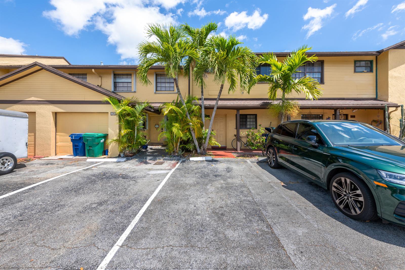 A two-story yellow townhouse with a driveway, palm trees, and a parked green car — 1129 NE 210th Terrace # 210, Miami FL 33179, MIAMI, FL