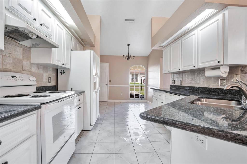 A galley-style kitchen features white cabinets, dark granite countertops, and light-colored tile flooring — 667 JESSANDA CIR, LAKELAND, FL