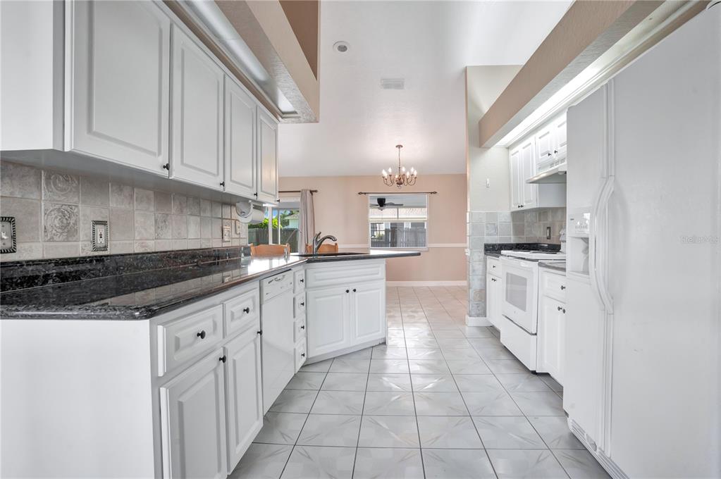 A kitchen with white cabinets, dark granite countertops, and white appliances leads to a dining area — 667 JESSANDA CIR, LAKELAND, FL