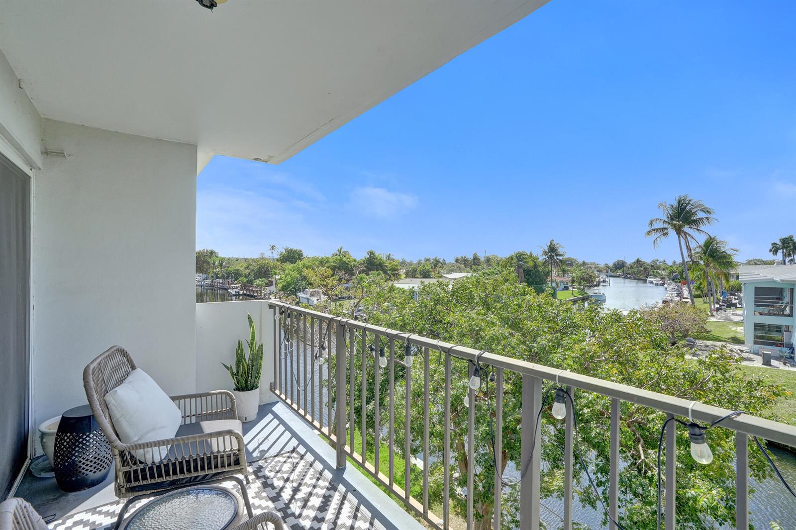 A balcony with a wicker chair overlooks a canal lined with trees and houses — 801 S Federal Highway # 301, Pompano Beach FL 33062, POMPANO BEACH, FL