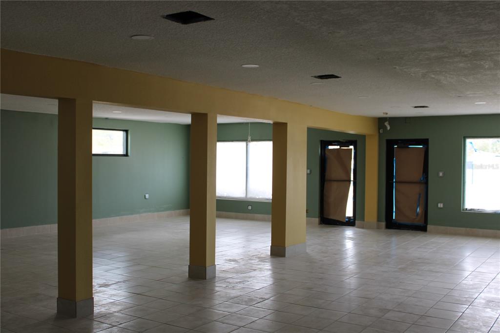An open, unfinished room features yellow support columns, green walls, and light-colored tile flooring — 2180 N HERCULES AVENUE, CLEARWATER, FL