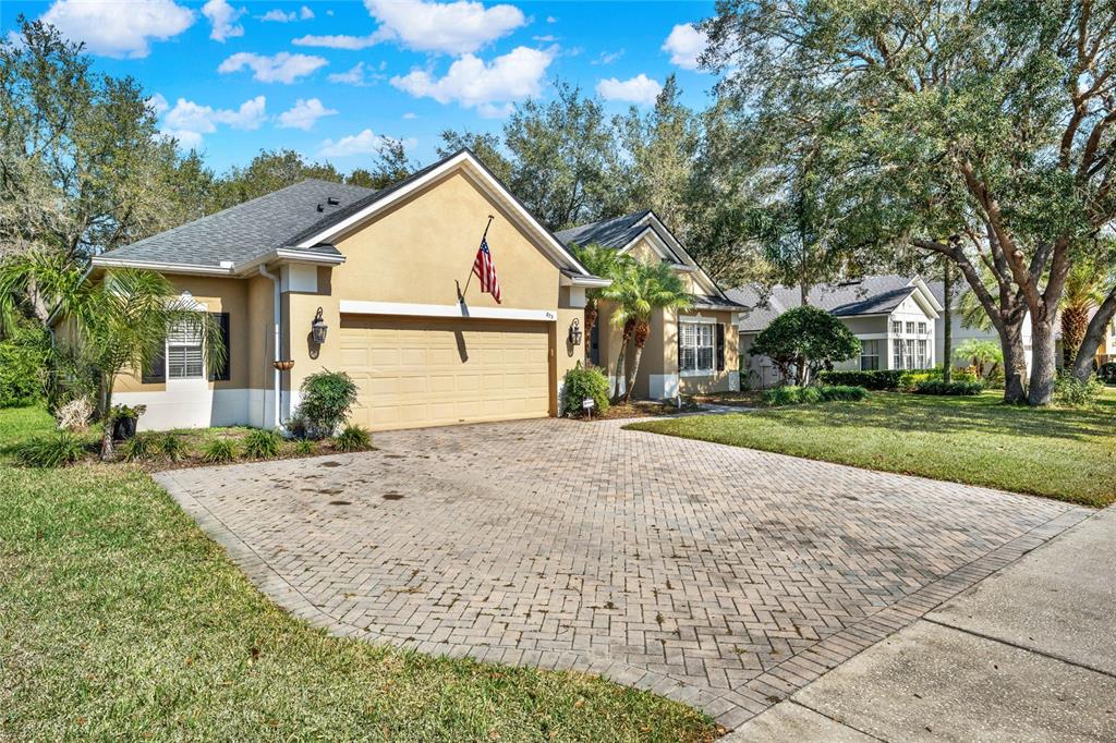 A tan single-story house with a paved driveway, a two-car garage, and mature trees — 873 GULF LAND DRIVE, APOPKA, FL