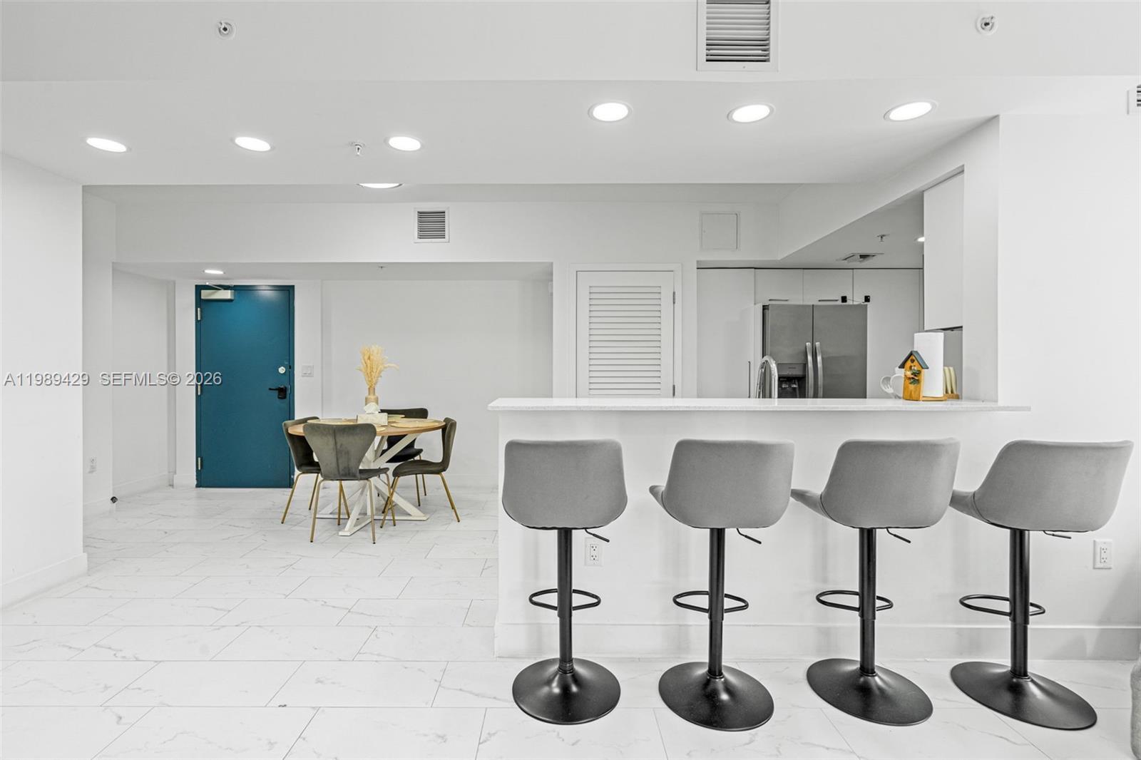 A modern kitchen features a white breakfast bar with four grey stools and tile flooring — 1850 Monroe Street # 309, Hollywood FL 33020, HOLLYWOOD, FL
