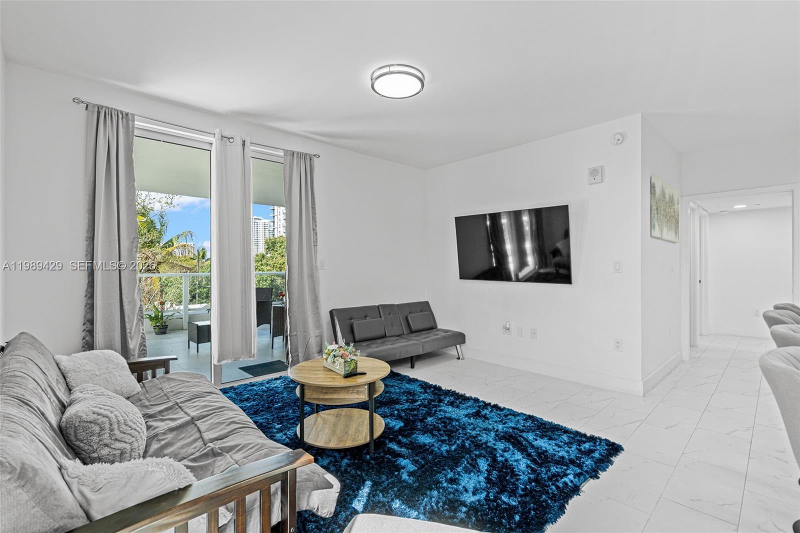 A living room features a blue shag rug, two gray sofas, and a balcony view — 1850 Monroe Street # 309, Hollywood FL 33020, HOLLYWOOD, FL